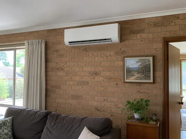 Wall-mounted split system running on a brick lounge room wall with curtains and framed art in Salisbury North