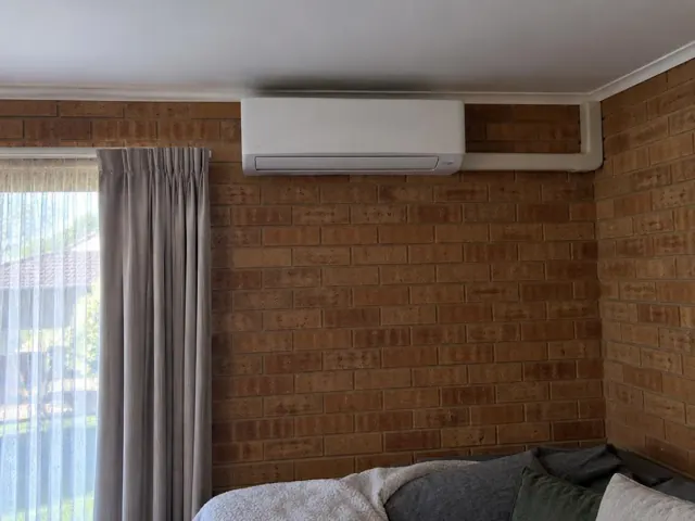 Split system mounted high on a brick bedroom wall above curtains and a bed in Salisbury Downs